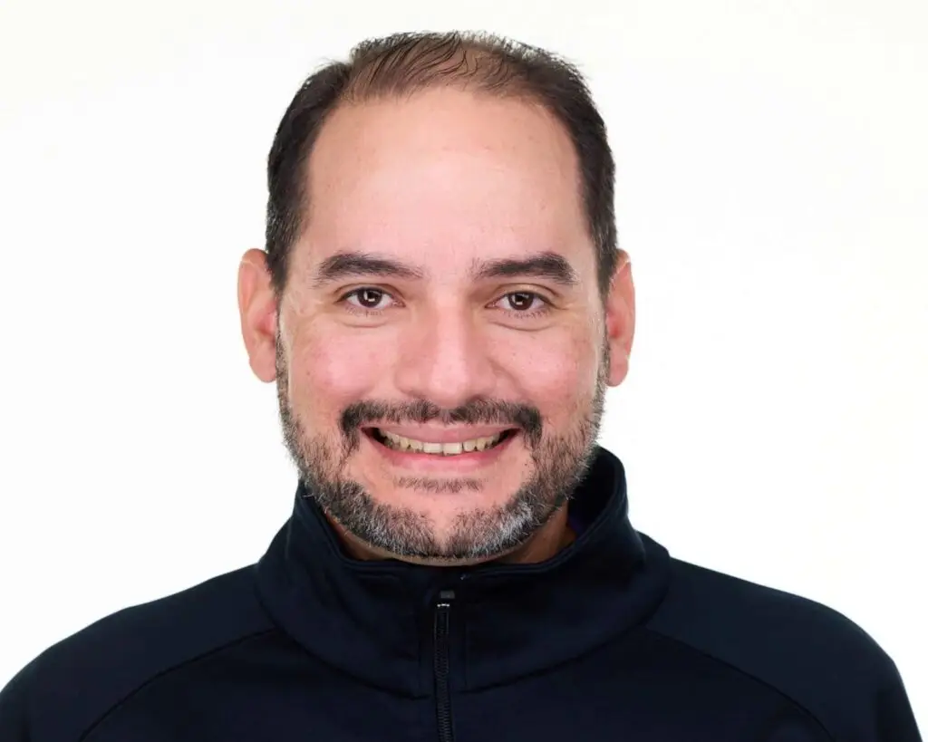 Smiling man with beard wearing dark zip-up jacket, studio headshot portrait